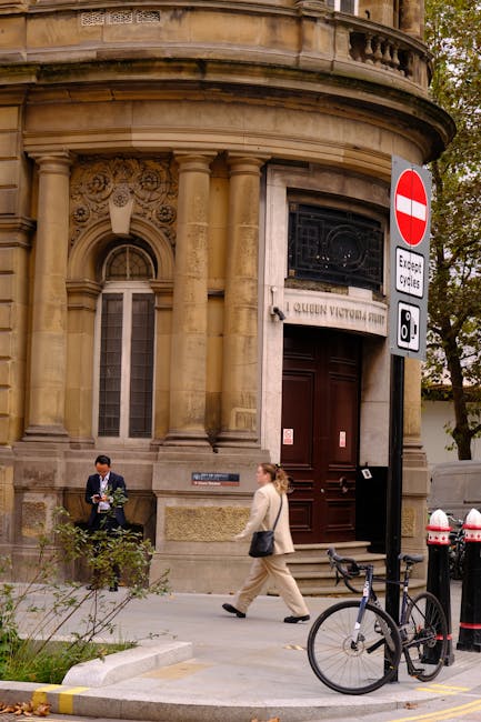 The image depicts a historic building on Queen Victoria Street with ornate architectural details, including decorative carvings and tall, rounded windows framed by classical columns. In front of the b